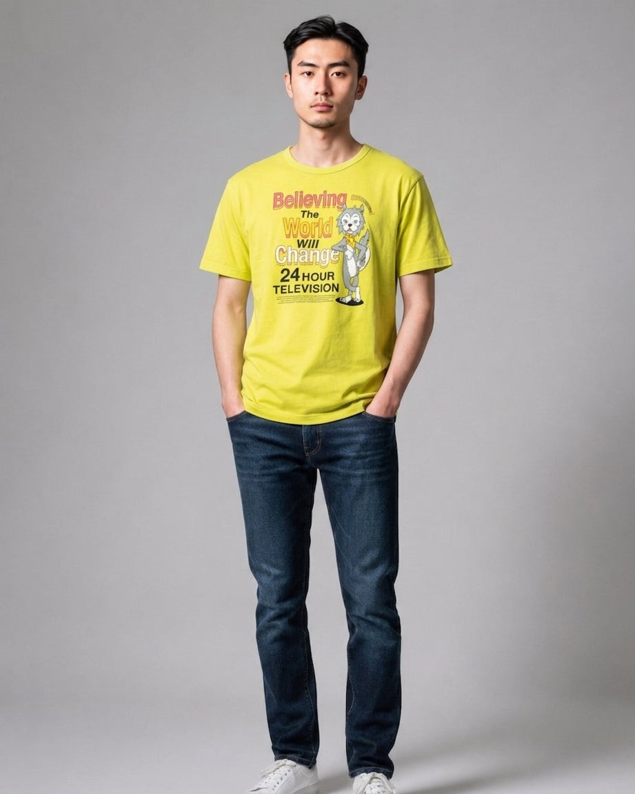 Man standing in full view wearing a yellow 24 Hour Television charity t-shirt with graphic print, dark blue jeans, and white sneakers