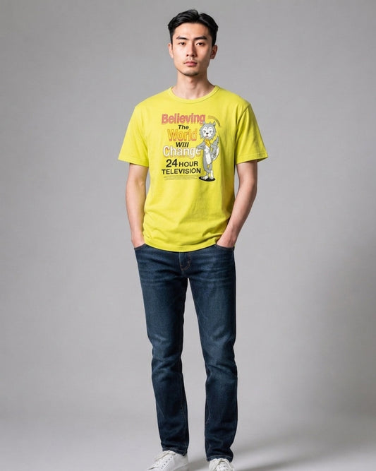 Man standing in full view wearing a yellow 24 Hour Television charity t-shirt with graphic print, dark blue jeans, and white sneakers