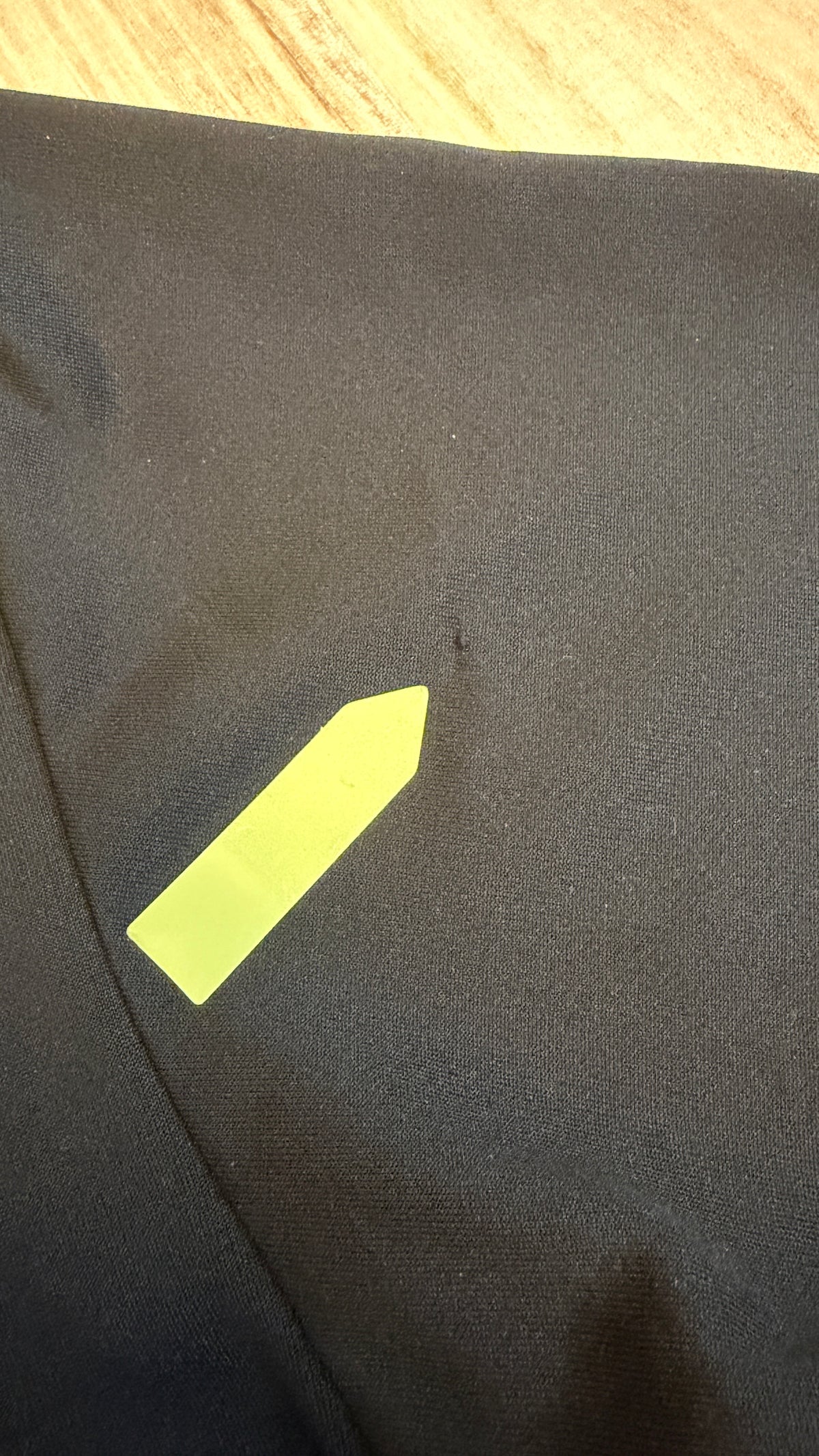 Close-up view of a black t-shirt showing a small fabric snag defect pointed out by a yellow sticker.