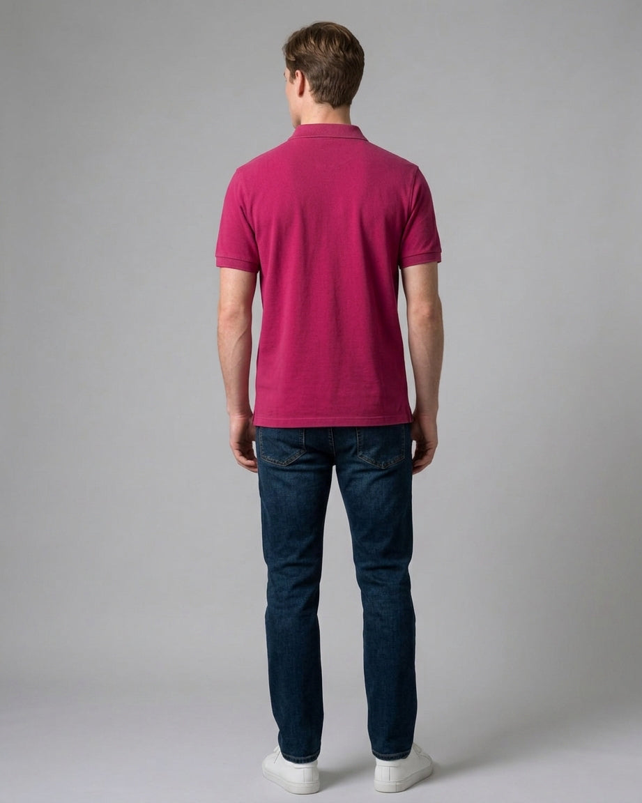 Man wearing a magenta pink short-sleeve polo shirt viewed from the back, styled with dark blue jeans and white sneakers