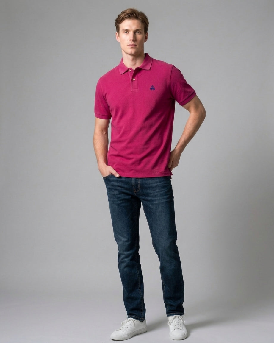 Man wearing a magenta pink Brooks Brothers polo shirt with a navy embroidered fleece logo on the chest, styled with dark blue jeans and white sneakers
