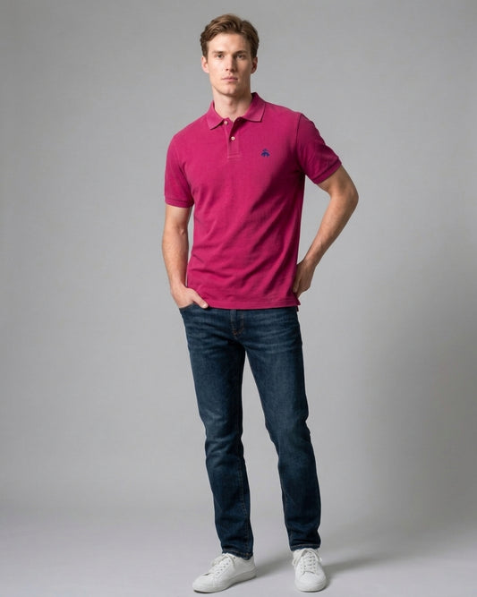 Man wearing a magenta pink Brooks Brothers polo shirt with a navy embroidered fleece logo on the chest, styled with dark blue jeans and white sneakers