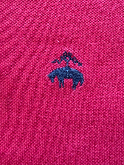 Close-up detail of the navy blue embroidered Brooks Brothers Golden Fleece sheep logo on magenta cotton pique fabric