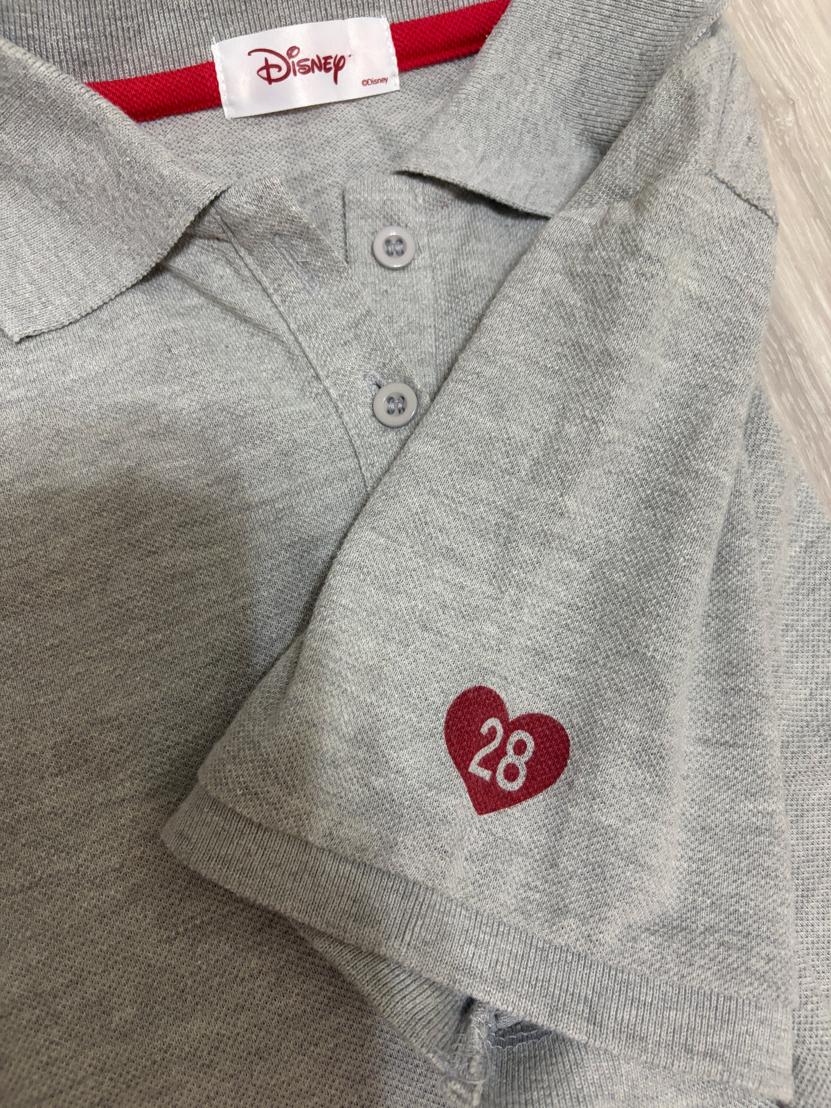Close-up detail of the red heart patch with number 28 embroidered on the sleeve of a heather grey polo shirt