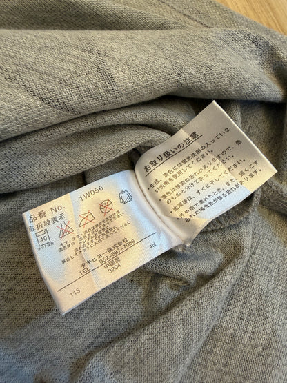 Close-up view of the inner white Japanese care tag on a grey polo shirt displaying item number 1W056, laundry symbols, and manufacturer Takihyo Co., Ltd. details