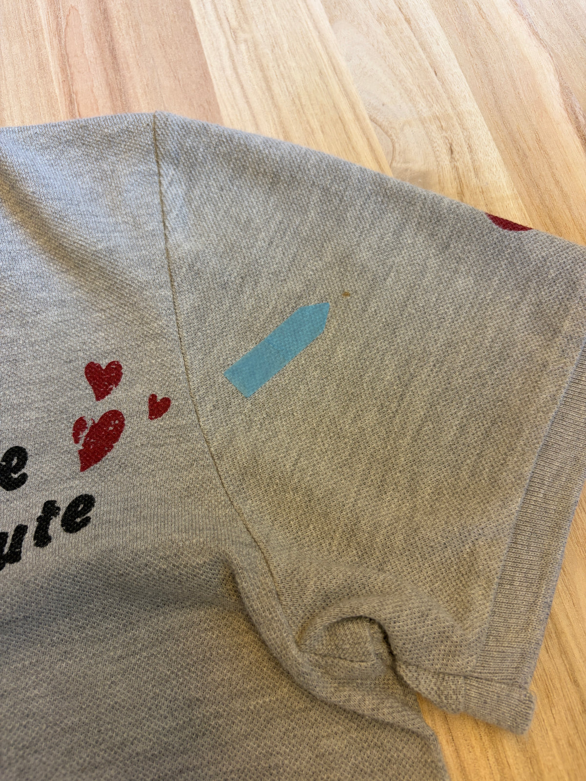 Close-up view of a grey Disney Minnie Mouse polo shirt shoulder seam showing a light brown stain defect marked with a blue sticker.