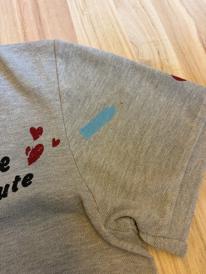 Close-up view of a grey Disney Minnie Mouse polo shirt shoulder seam showing a light brown stain defect marked with a blue sticker.