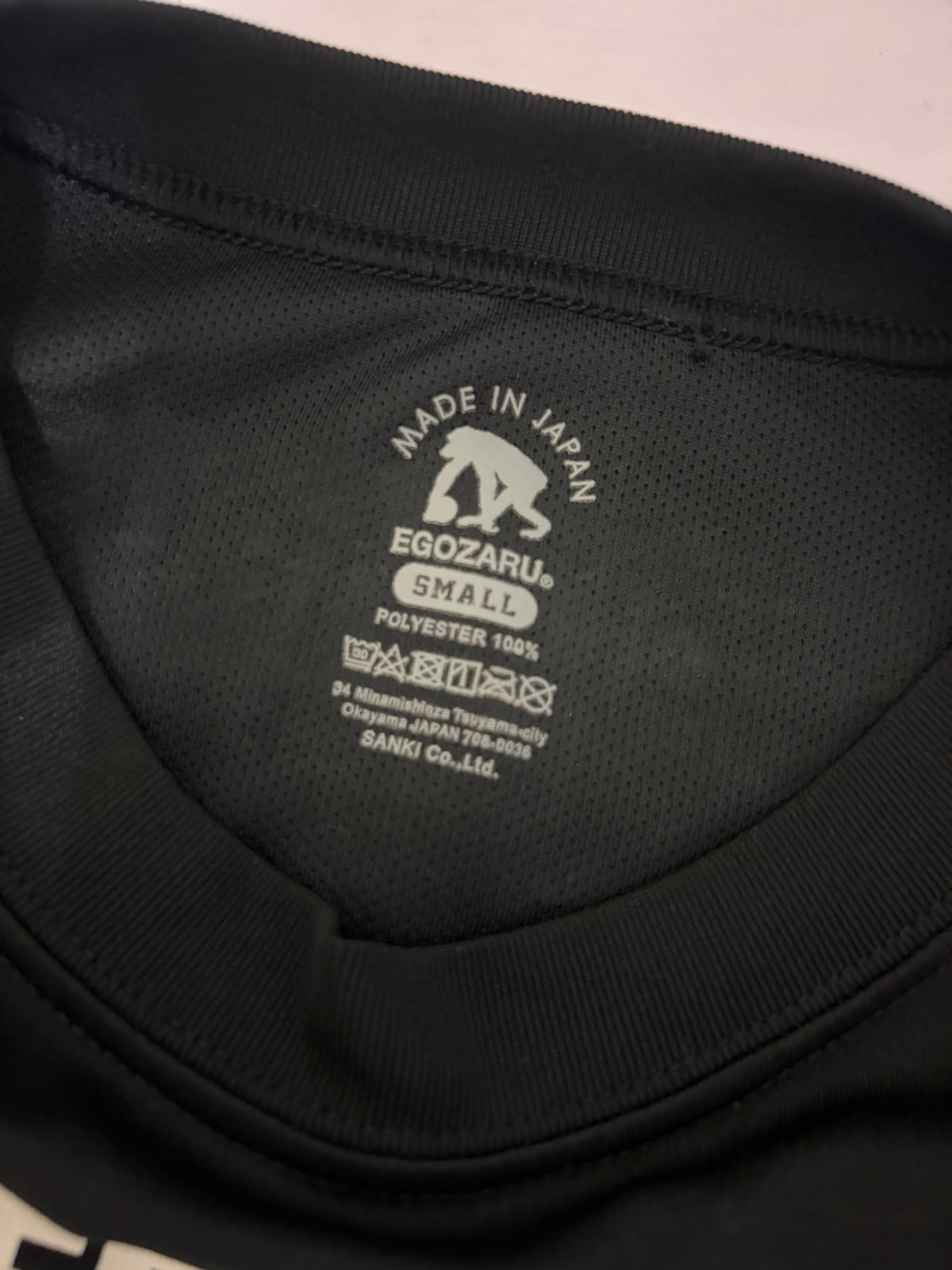 Close-up detail of the white Egozaru box logo printed on the upper back neckline of a black sports t-shirt
