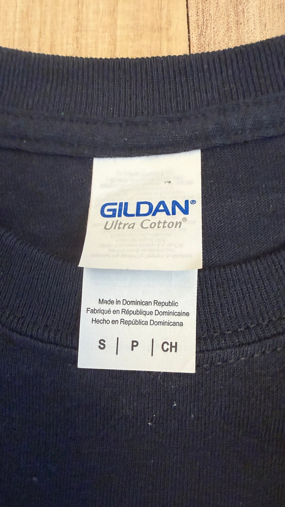 Close-up view of a white Gildan Ultra Cotton brand collar label inside a black t-shirt indicating size Small and Made in Dominican Republic