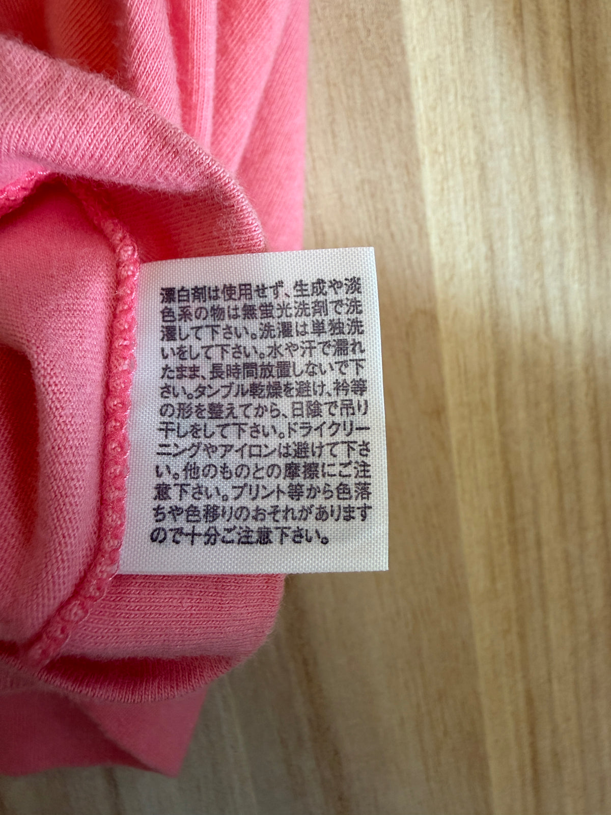 Close-up view of the reverse side of an inner white fabric care tag on a pink t-shirt displaying Japanese text instructions for washing, drying, and ironing graphic prints
