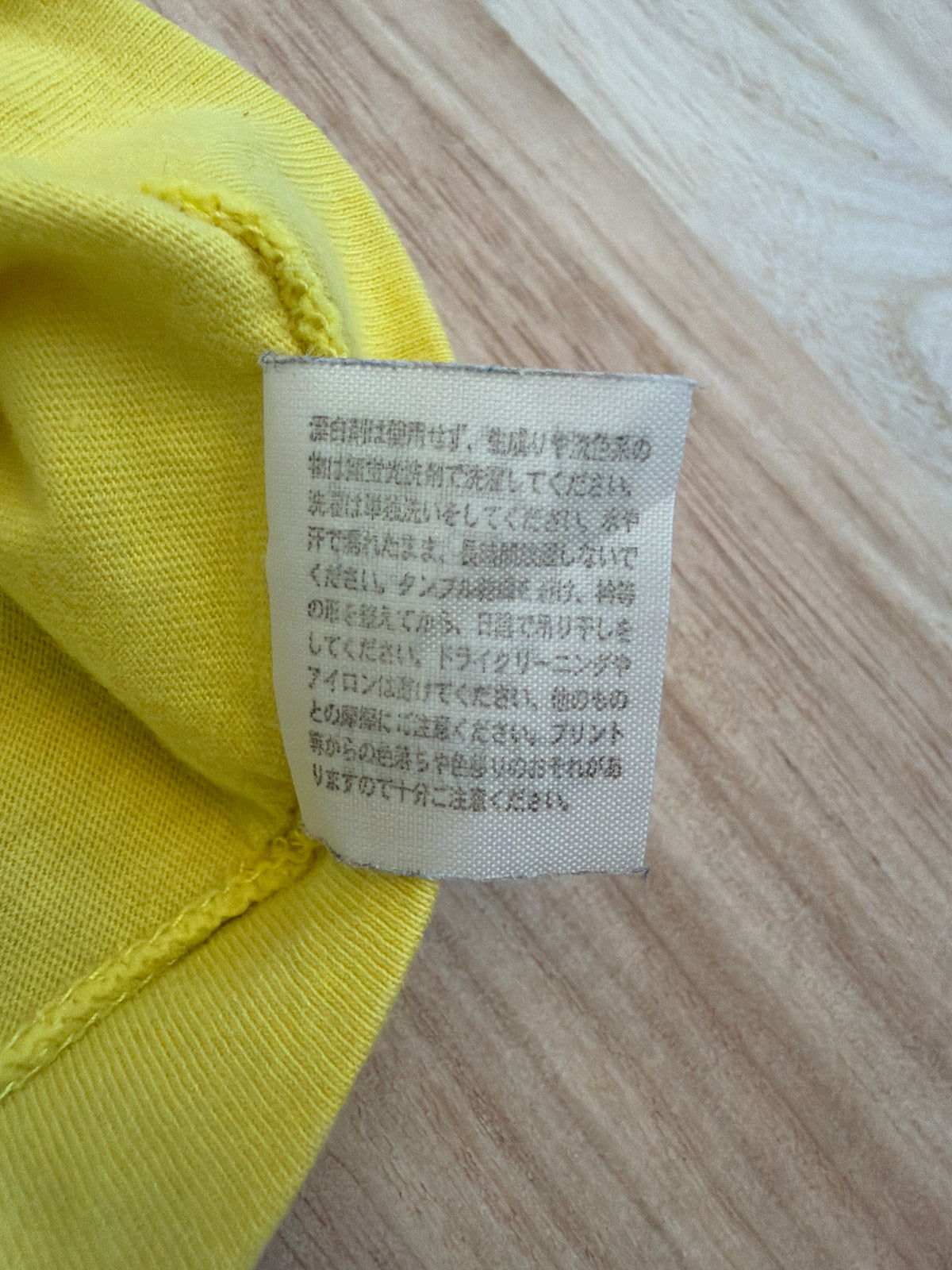 Close-up view of the reverse side of an inner white fabric care tag on a yellow t-shirt displaying Japanese text instructions for washing, drying, and print maintenance