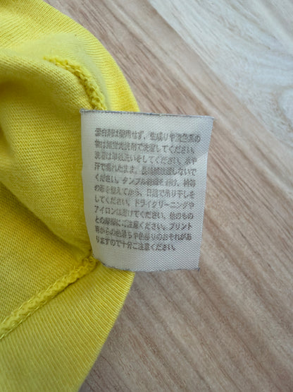 Close-up view of the reverse side of an inner white fabric care tag on a yellow t-shirt displaying Japanese text instructions for washing, drying, and print maintenance