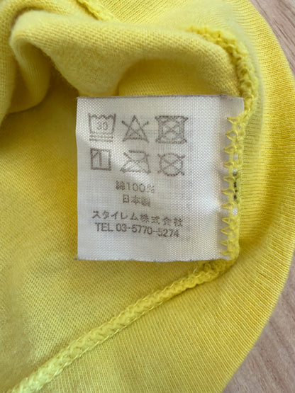 Close-up view of the inner white fabric tag on a yellow t-shirt showing Japanese care symbols, 100% cotton material composition, Made in Japan, and Stylem Co., Ltd. distributor details