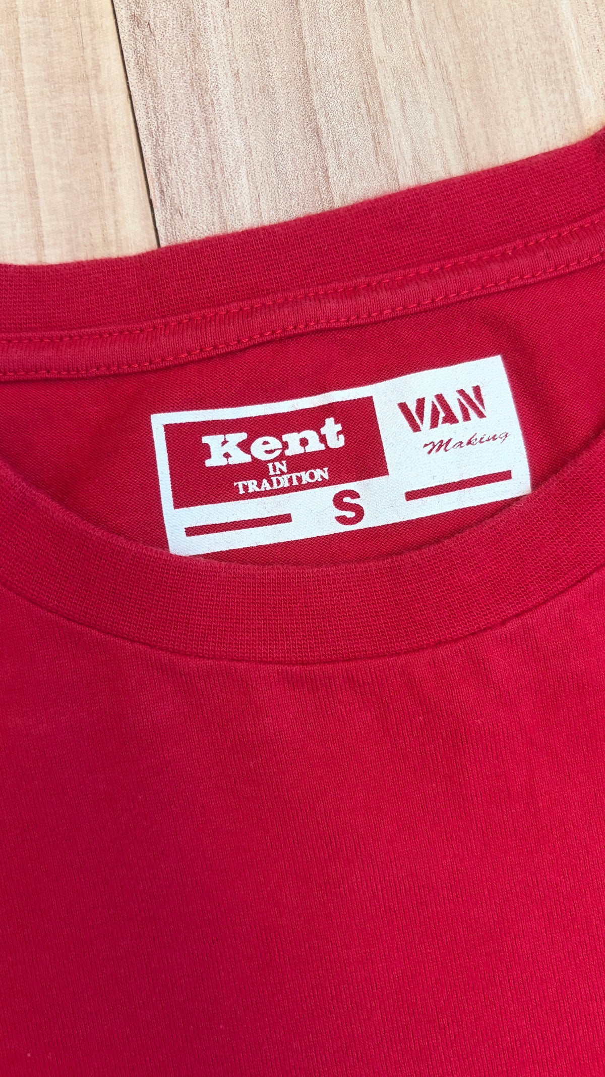 Close-up view of the inner back collar of a red t-shirt featuring a white printed label with red text reading Kent IN TRADITION, VAN, and size S