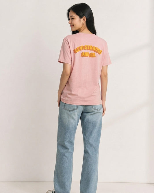 Woman wearing dusty pink Levi Strauss and Co. t-shirt showing yellow arch logo on the back, paired with light denim jeans