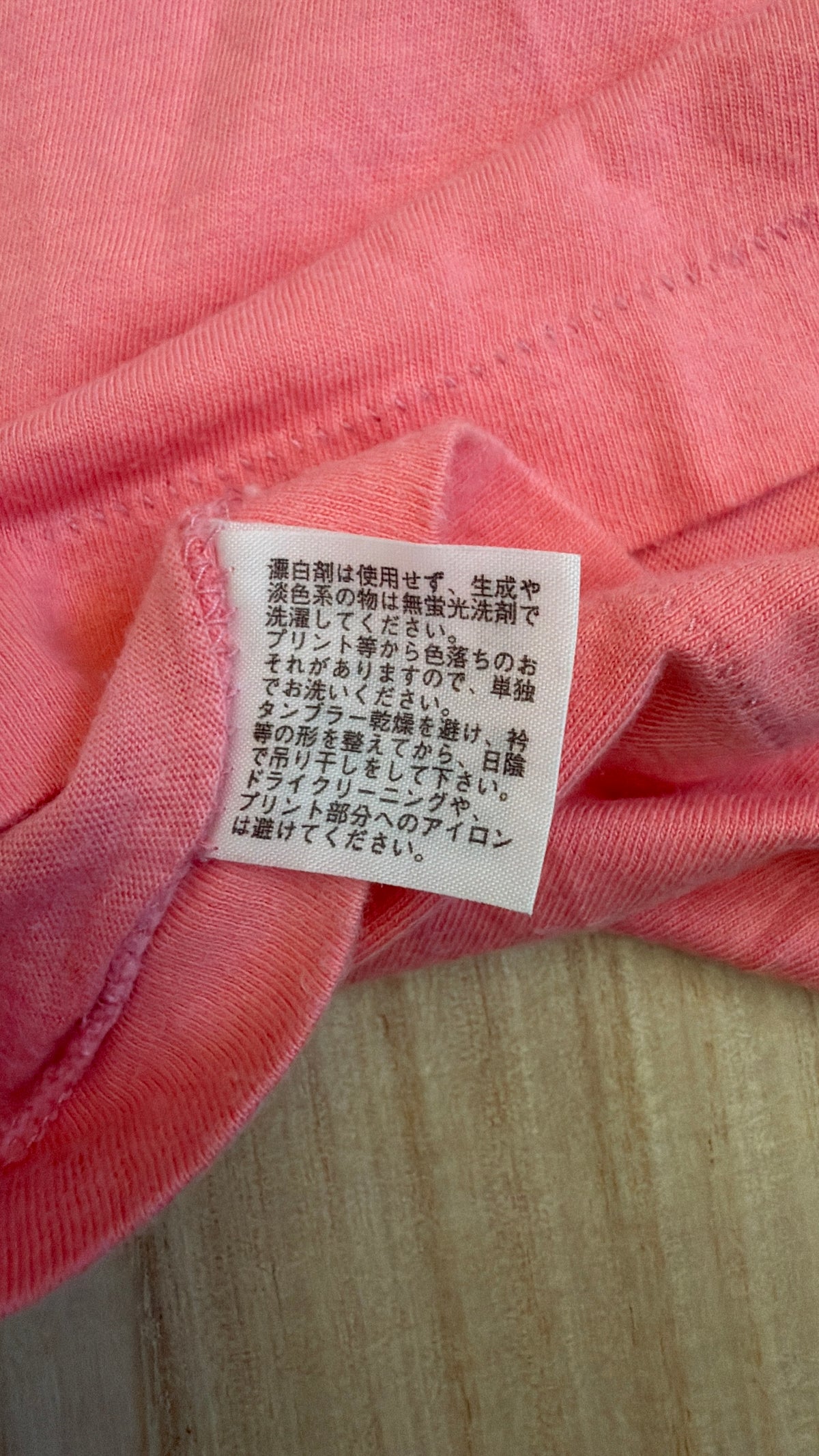 Close-up view of the reverse side of an inner white fabric tag on a pink t-shirt showing Japanese care instructions for washing, drying, and ironing