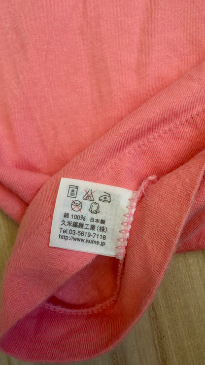 Close-up view of the inner white fabric tag on a pink t-shirt displaying laundry icons, 100% cotton composition, Made in Japan, and Kume Sen-i Co., Ltd. manufacturer details