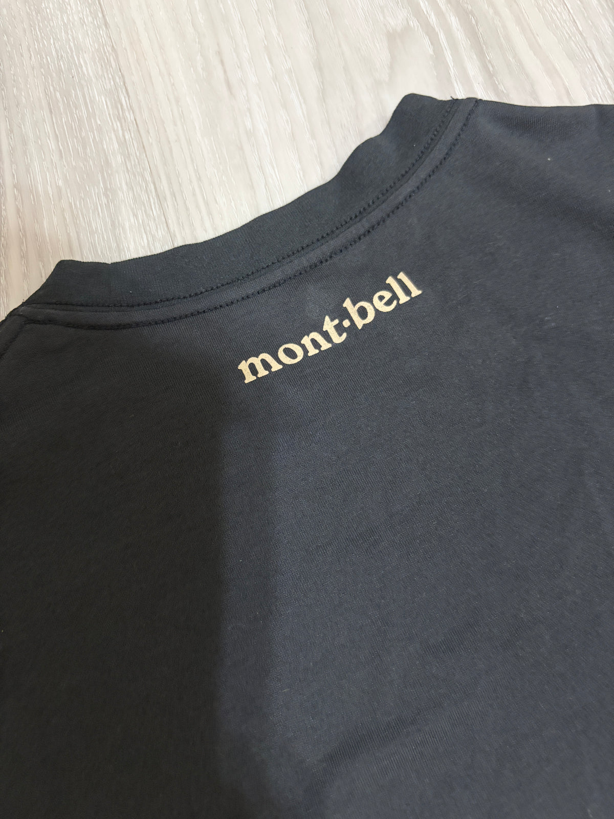Close-up detail of the cream Montbell logo printed on the upper back neck of a black t-shirt