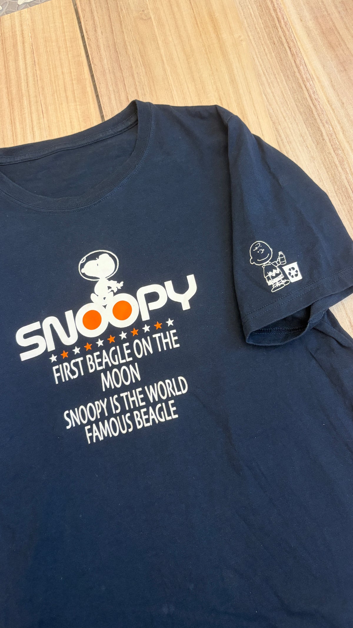 Navy blue Peanuts t-shirt printed with Snoopy in an astronaut helmet above text reading First Beagle on the Moon with Charlie Brown graphic on the sleeve