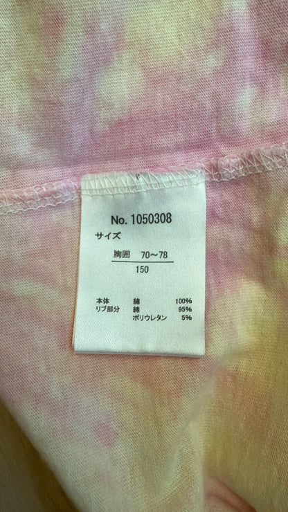 Close-up view of the inner white Japanese tag on a pastel tie-dye t-shirt showing style number 1050308, size 150 for chest size 70-78 cm, and material composition of 100% cotton body with 95% cotton and 5% polyurethane ribbing