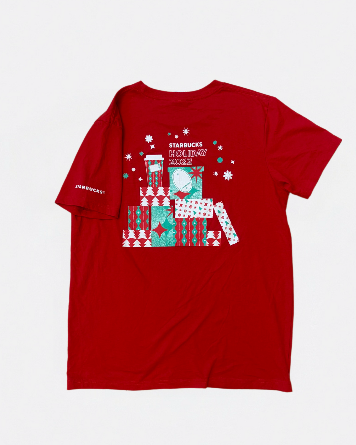 Red Starbucks short-sleeve t-shirt with a back print graphic featuring stacked holiday gifts, a coffee cup, snowflakes, and Starbucks Holiday 2022 text laid flat