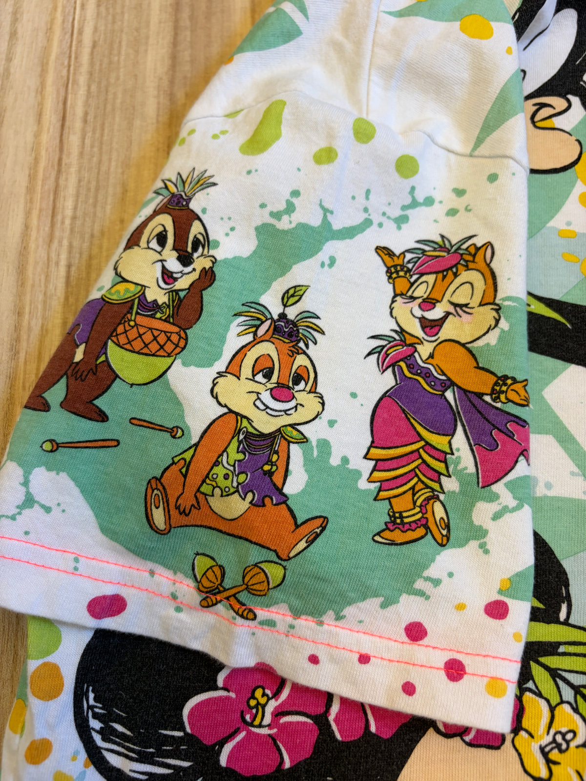 Close-up view of a short sleeve on a colorful all-over print t-shirt featuring Disney characters Chip, Dale, and Clarice in tropical outfits