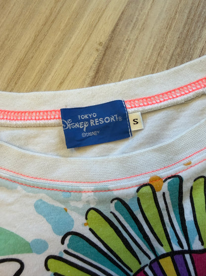 Close-up view of the inner neck collar on a white graphic t-shirt displaying a blue Tokyo Disney Resort woven tag with size S