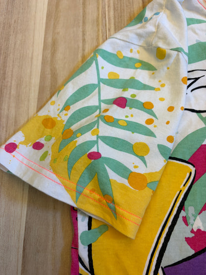 Close-up view of a short sleeve on an all-over print t-shirt showing green tropical leaves and yellow and pink paint splatters