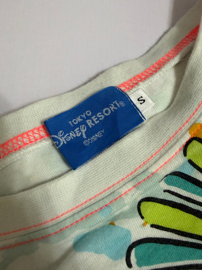 Close-up detail of the blue Tokyo Disney Resort neck label and size S tag on the white all-over print t-shirt with pink collar stitching.
