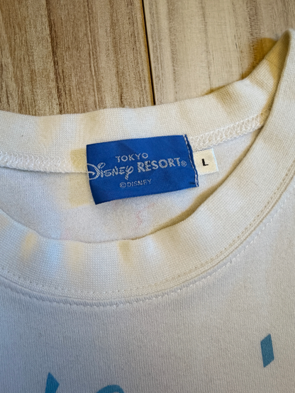 Close-up view of the inner neck collar on a white graphic t-shirt displaying a blue Tokyo Disney Resort woven label with size L