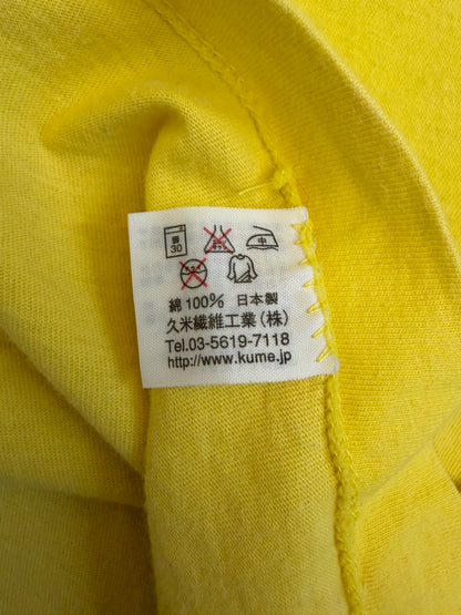 Close-up view of the inner white fabric tag on a yellow t-shirt showing Japanese care symbols, 100% cotton composition, Made in Japan, and Kume Sen-i Co., Ltd. manufacturer details