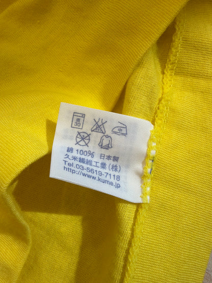 Close-up view of the inner white fabric care tag on a yellow t-shirt displaying laundry icons, 100% cotton composition, Made in Japan, and manufacturer Kume Sen-i Co., Ltd. details